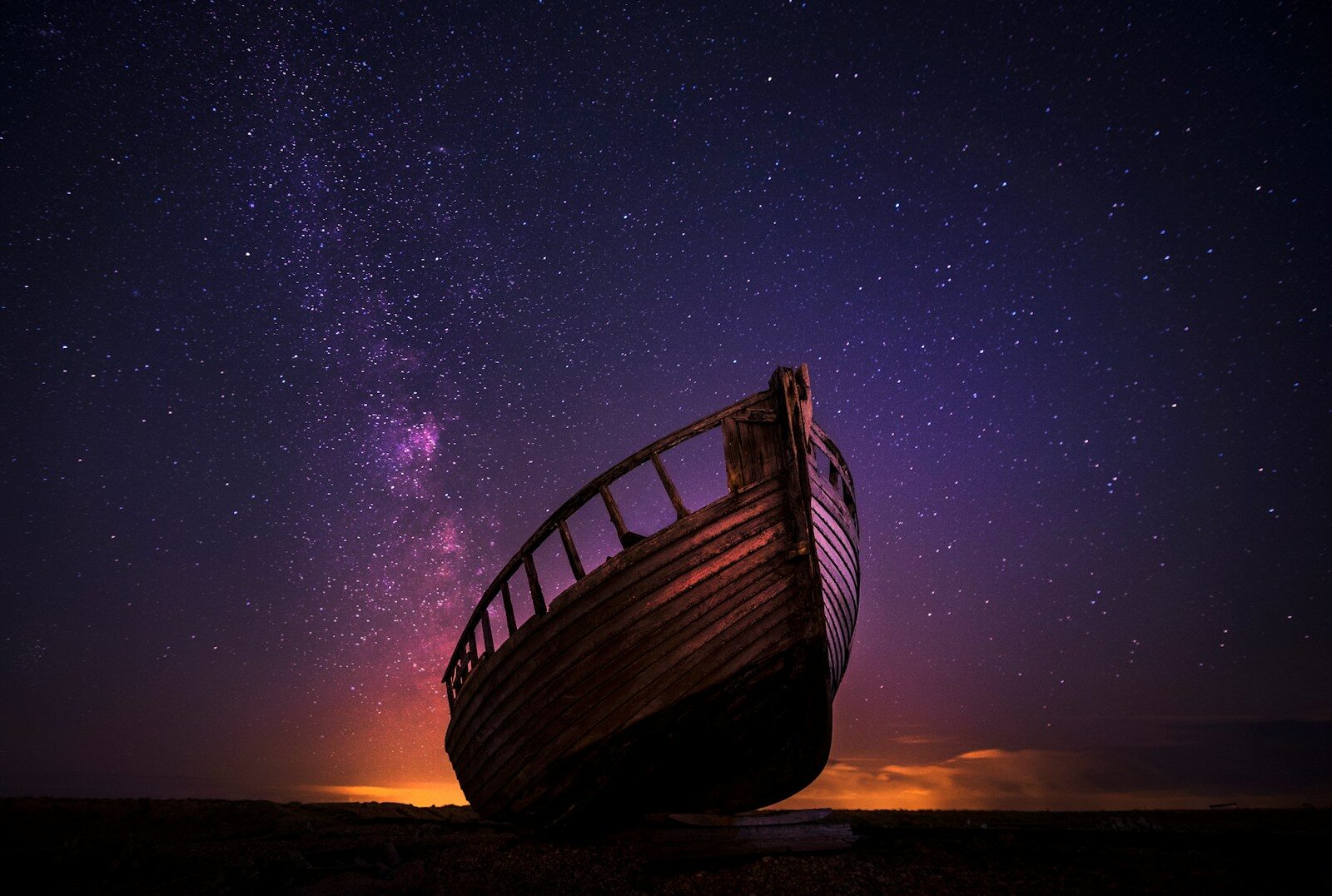 An old wooden boat hull silhouetted against a vibrant purple starry night sky